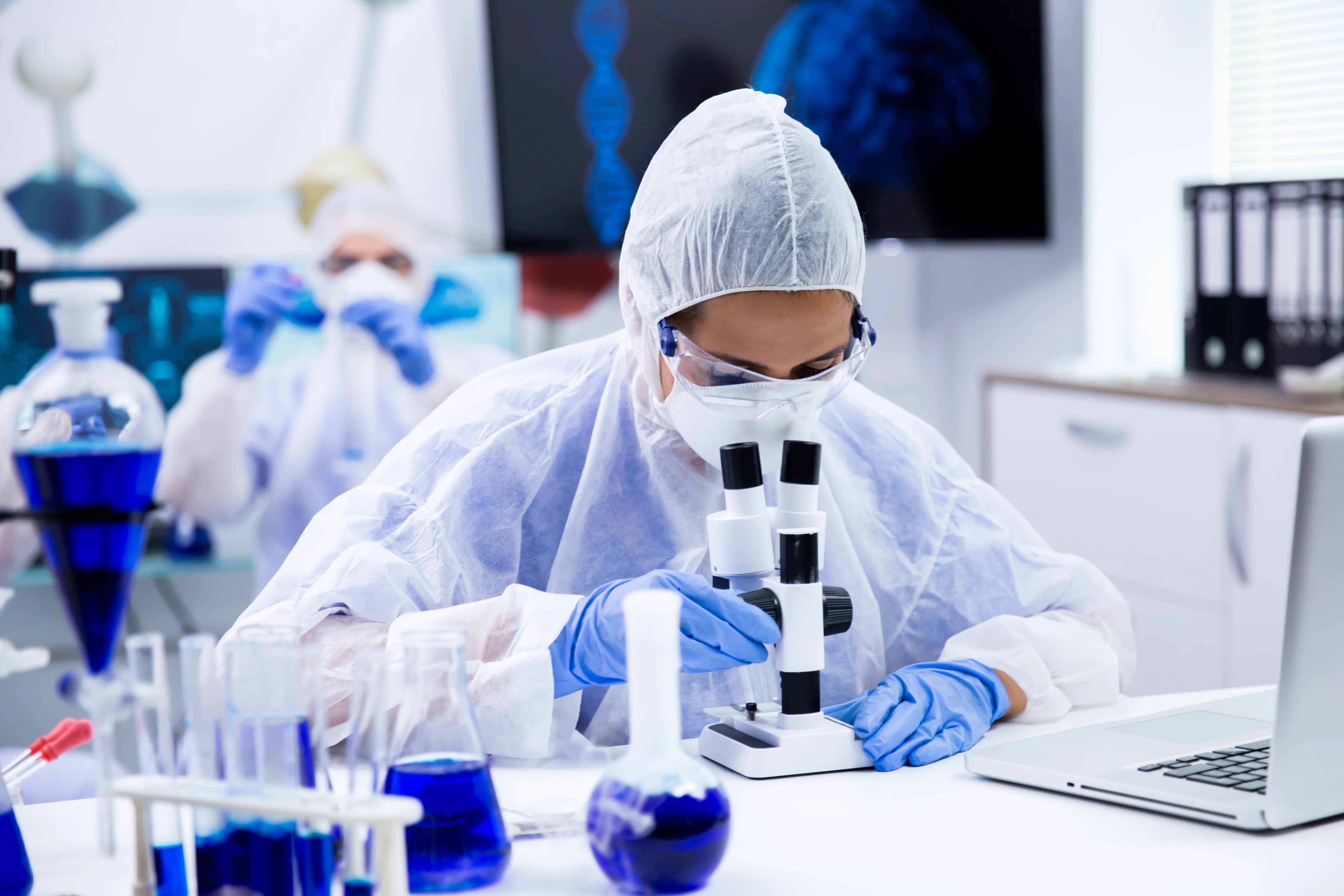 Scientist at microscope with blue test tubes